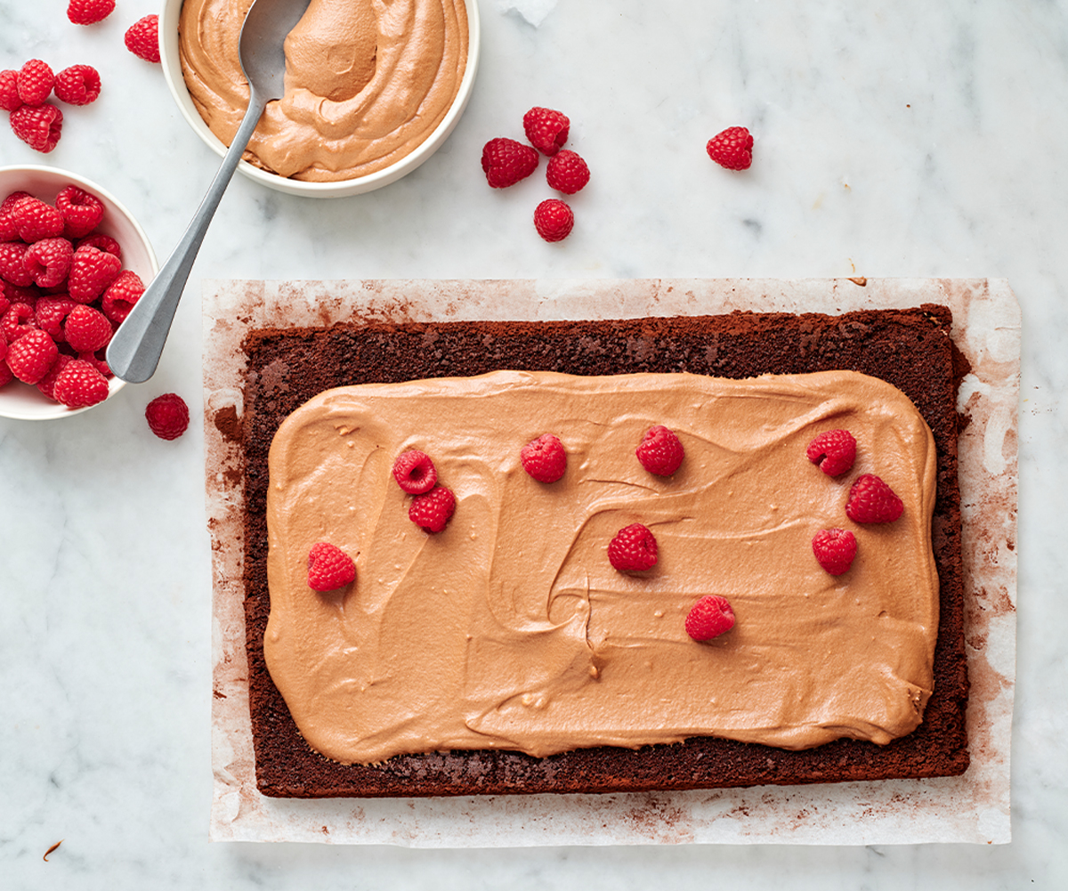 chocolate yule log sponge with light brown chocolate cream on top, scattered with raspberries