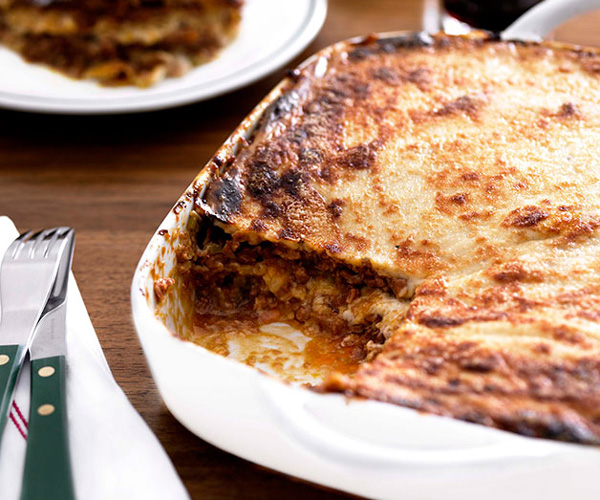 A white baking tray with lasagne, with a rectangle slice cut out.