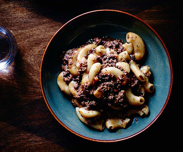 A bowl of pasta with ground meat sauce on a wooden table.