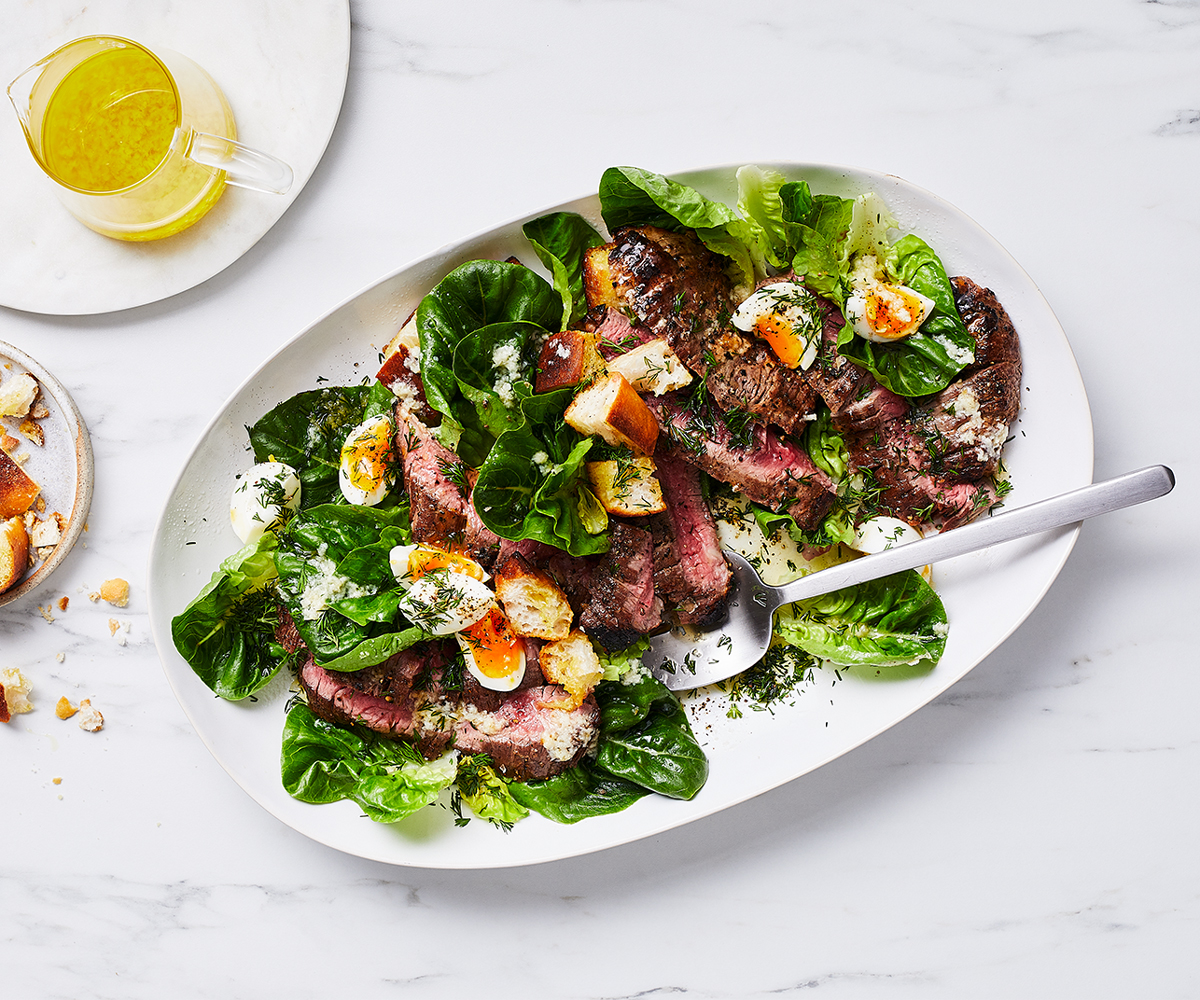 An aerial view of an oval platter filled with grilled chopped pepper steak with baby lettuce salad.