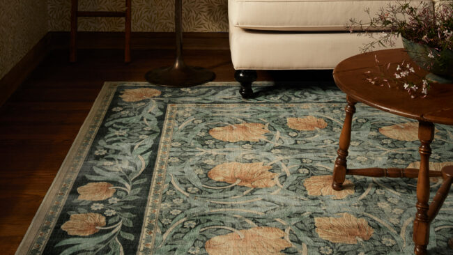 Lifestyle photo showing Ruggable x Morris & Co. blueish green rug with pink flowers with dark timber coffee table