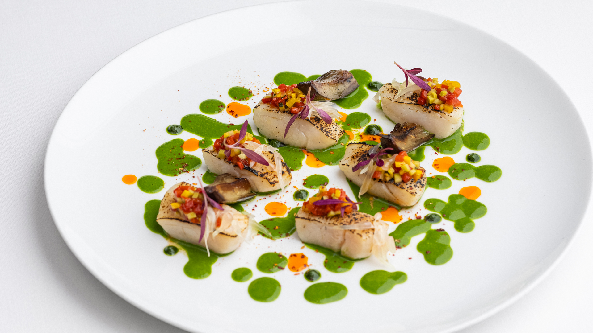 Six Hokkaido scallops on white plate with green sauce splodges and pruple and yellow garnish at Michelin Guide restaurant Arcane in Hong Kong
