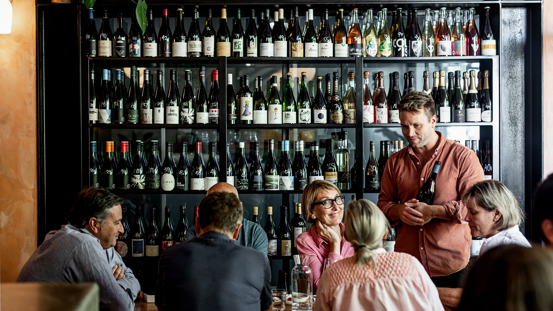 People sitting at a bar infront of a wall of wine