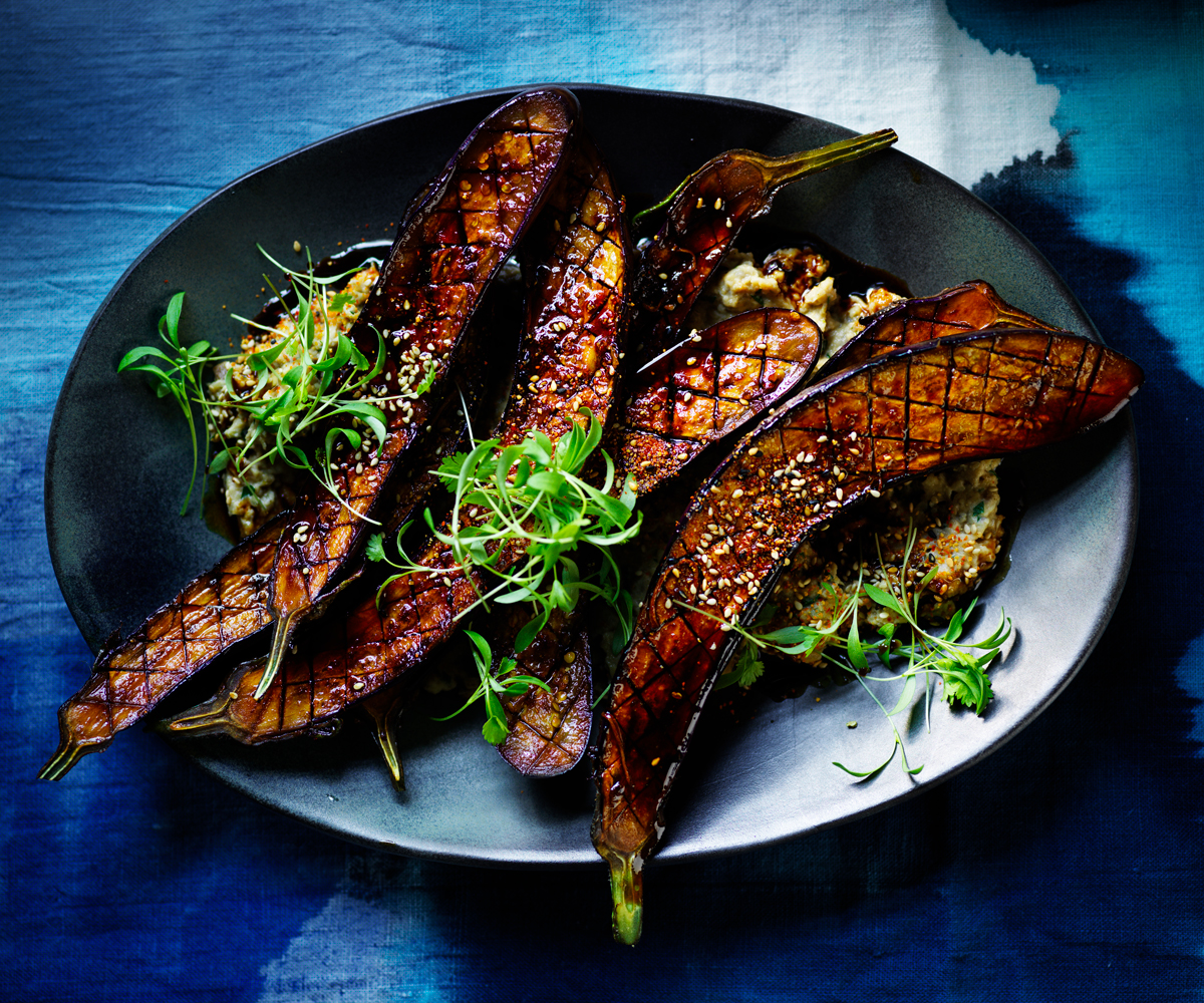 Four grilled Japanese eggplant slices, on a blue plate with a blue background. 