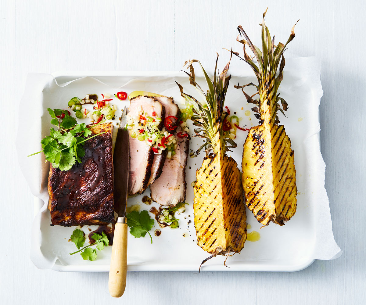 bird's eye view of pork fillet and sliced pork and two charred pineapple quarters on a white tray